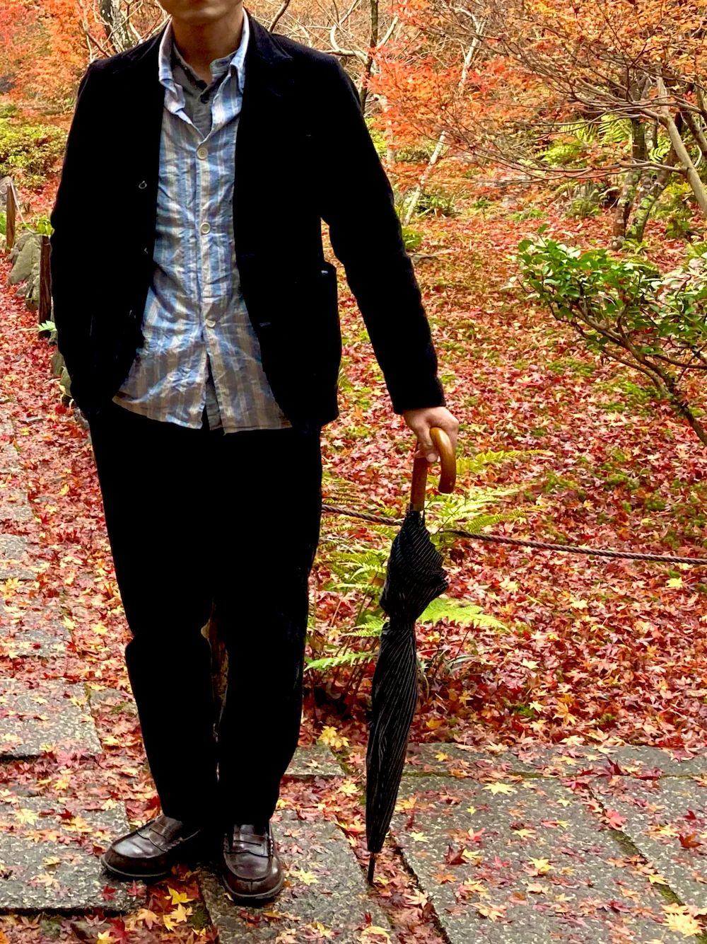 紅葉の遊歩道で撮影された男性の秋コーデ。ジャケットとローファーを合わせ、旅行シーンにぴったり。