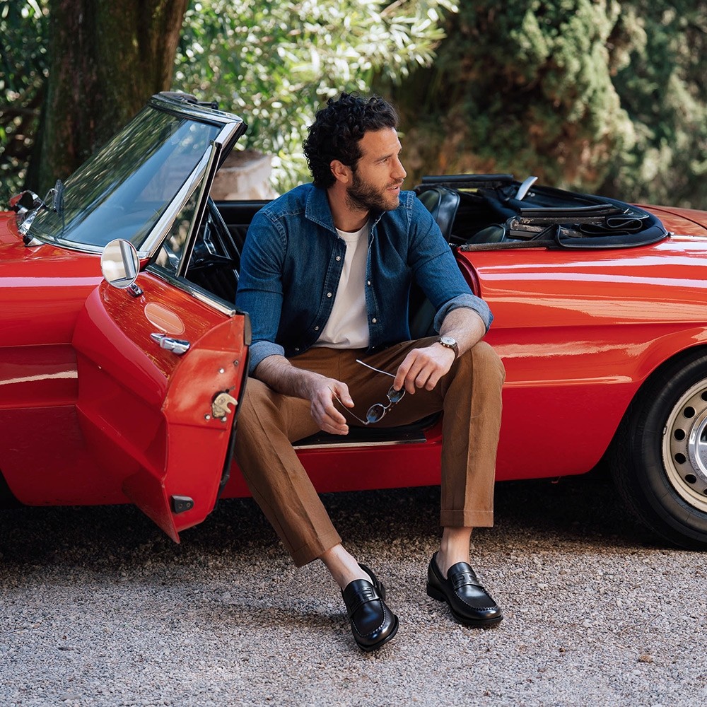 Mann im Smart-Casual-Look mit schwarzen Loafern neben Cabrio – Schuhe, die größer machen im Freizeitstil.