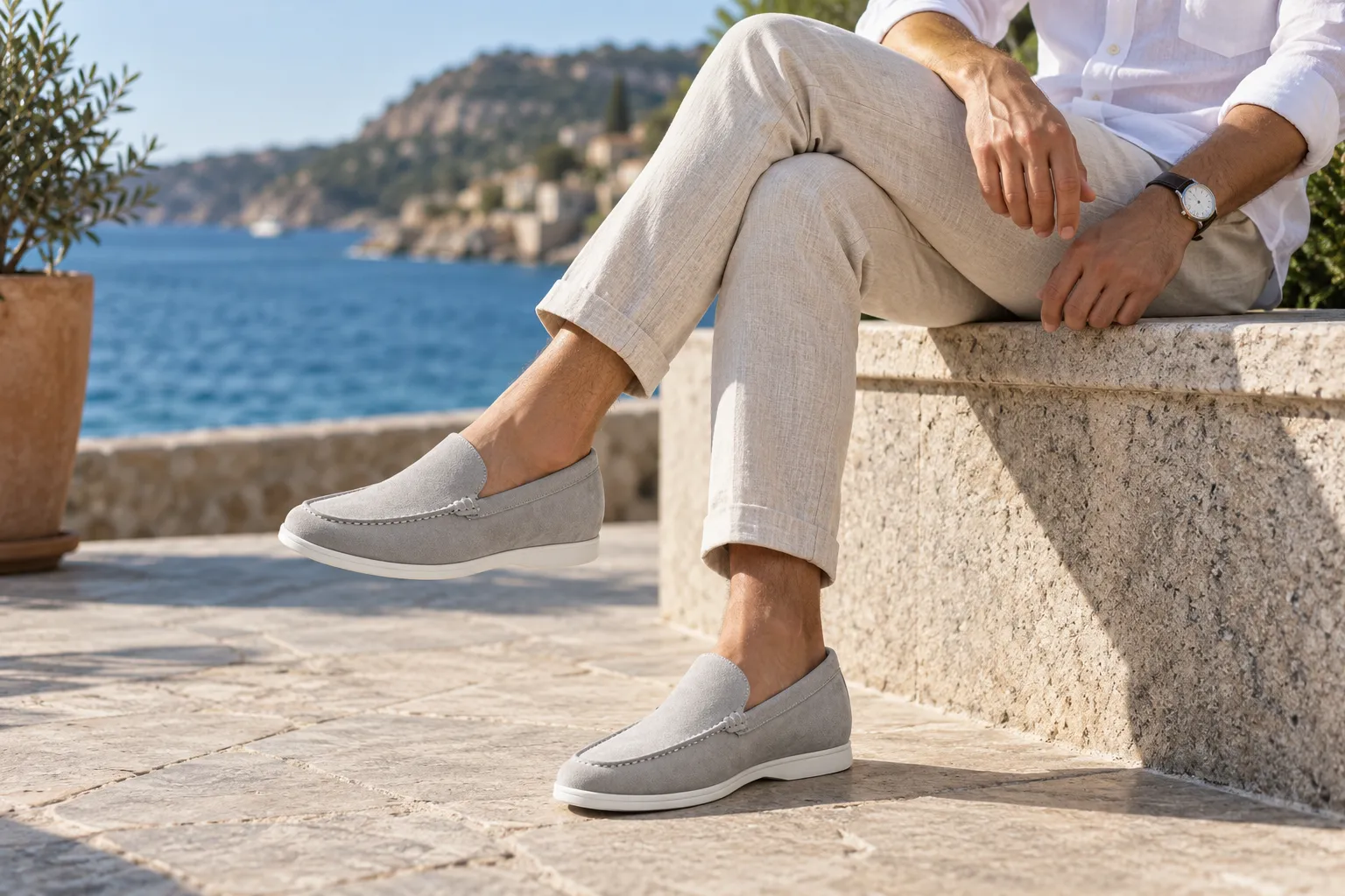 A man wearing natural linen trousers, a white shirt, and grey suede casual elevator loafers, sitting by the coast in Australia during summer, showcasing a relaxed smart-casual look.