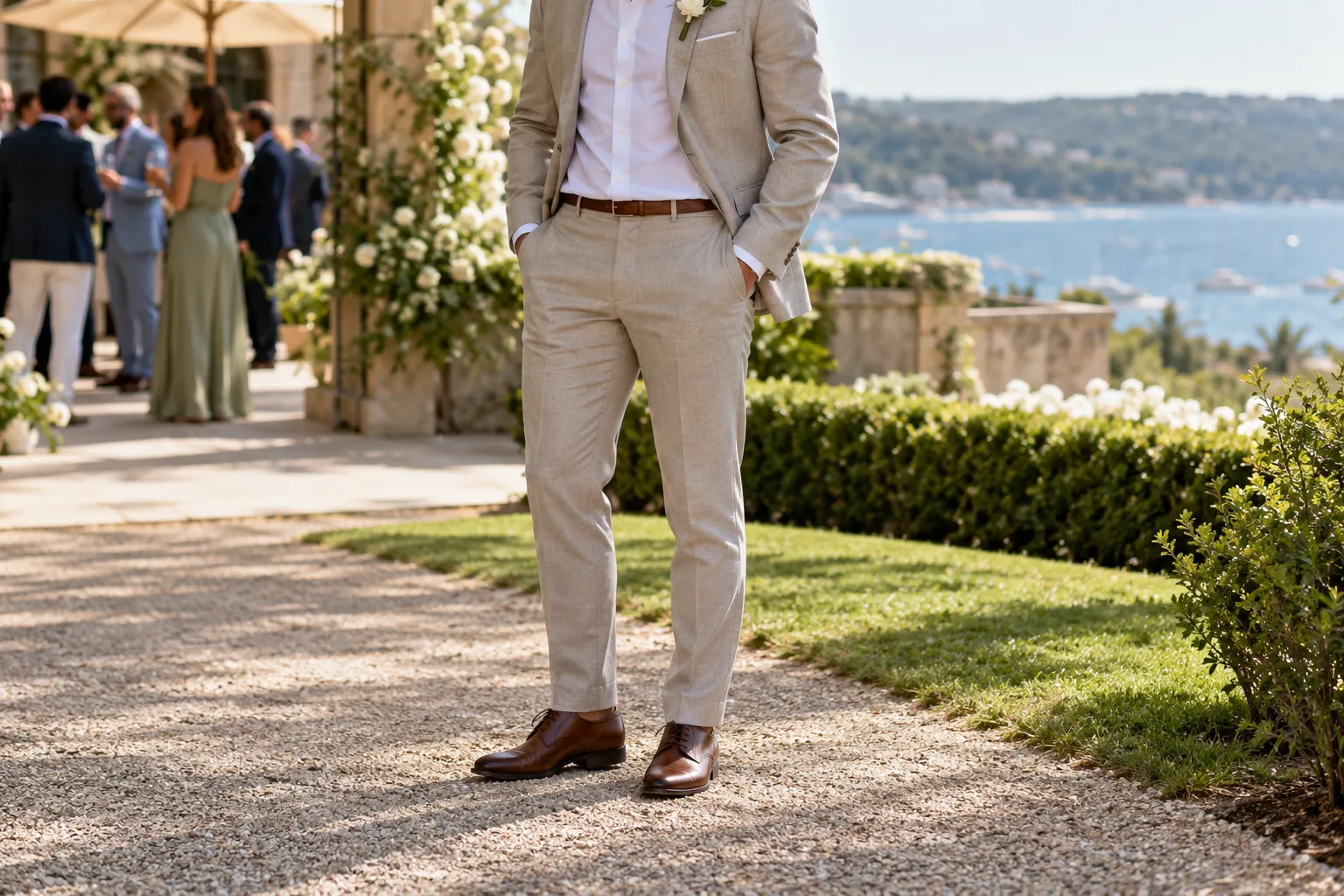 Man in a stone-coloured summer suit with a brown leather belt and brown leather oxford shoes on a garden gravel path